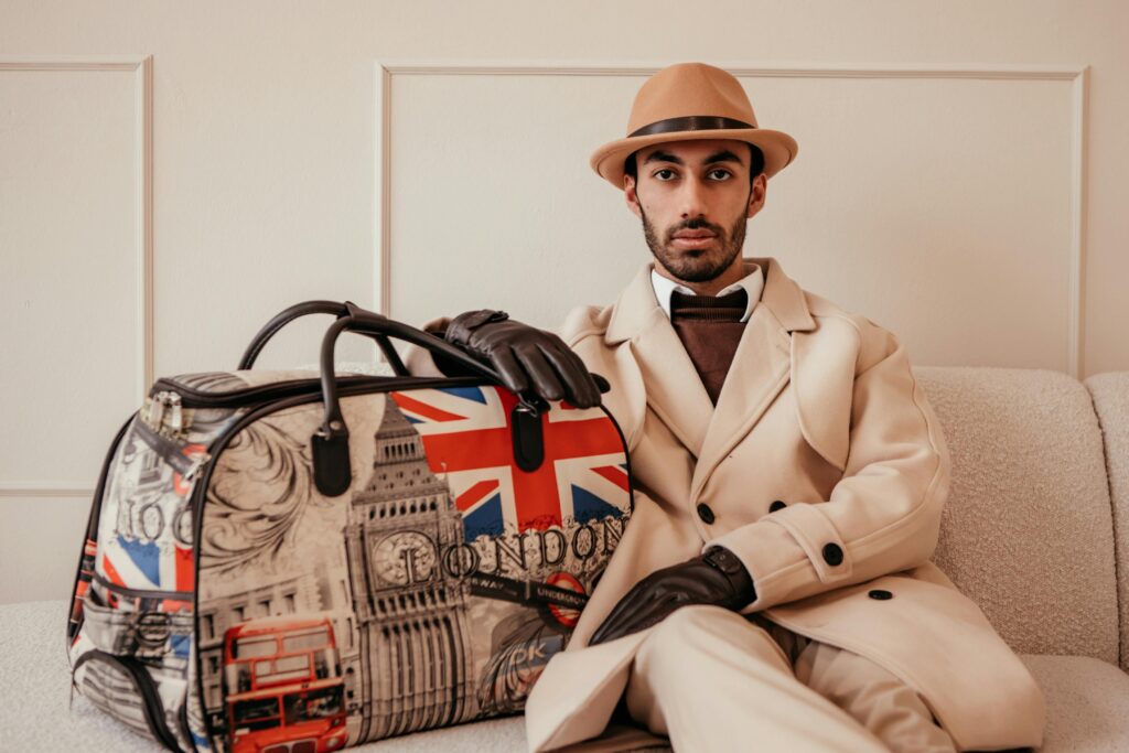 Stylish man in beige coat and hat holding a London-themed bag indoors.